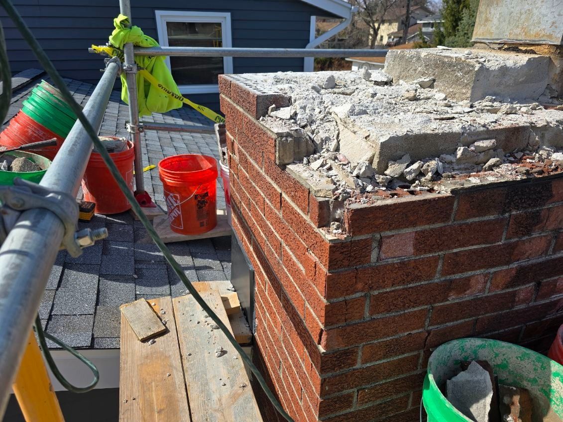 Chimney under construction on a rooftop with brick and concrete damage, scaffolding, and buckets.