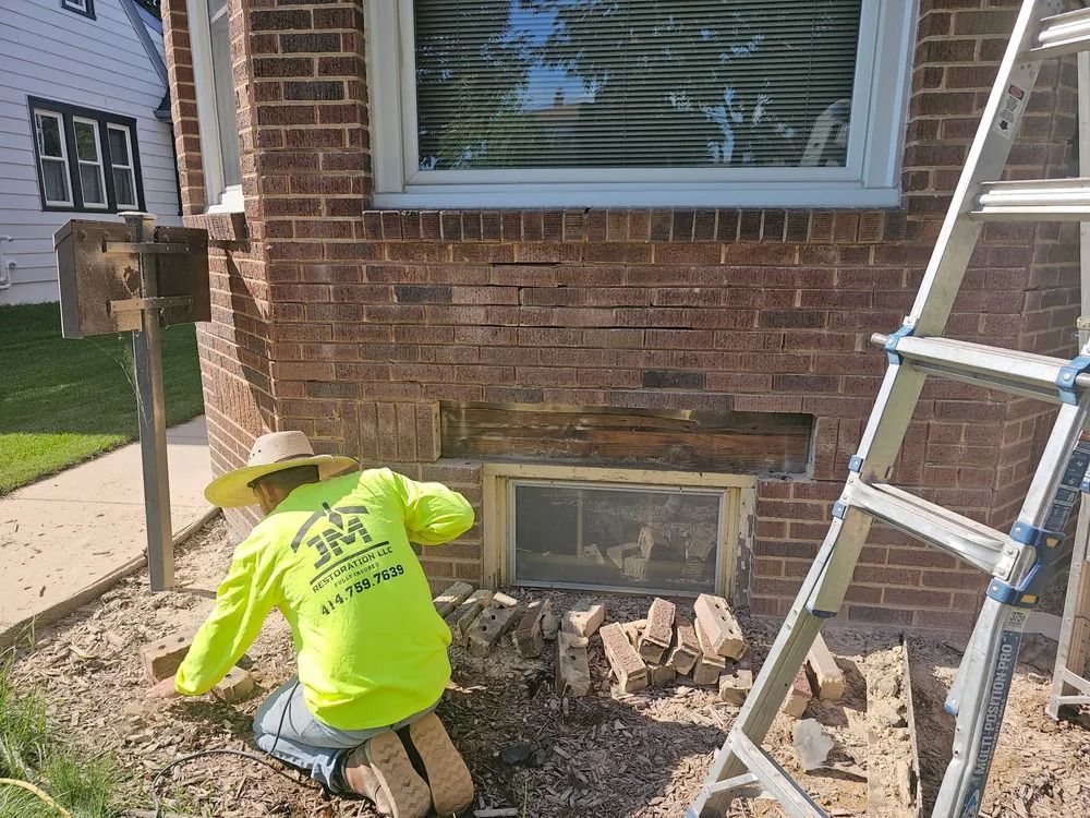 Person in neon yellow shirt repairing brick wall. Bricks and ladder visible.