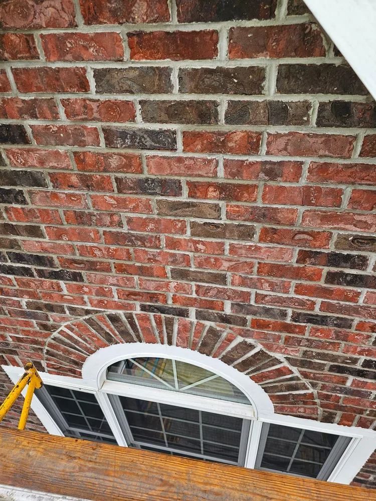 Brick exterior with arched window, red and brown bricks, white trim, and a glimpse of scaffolding.