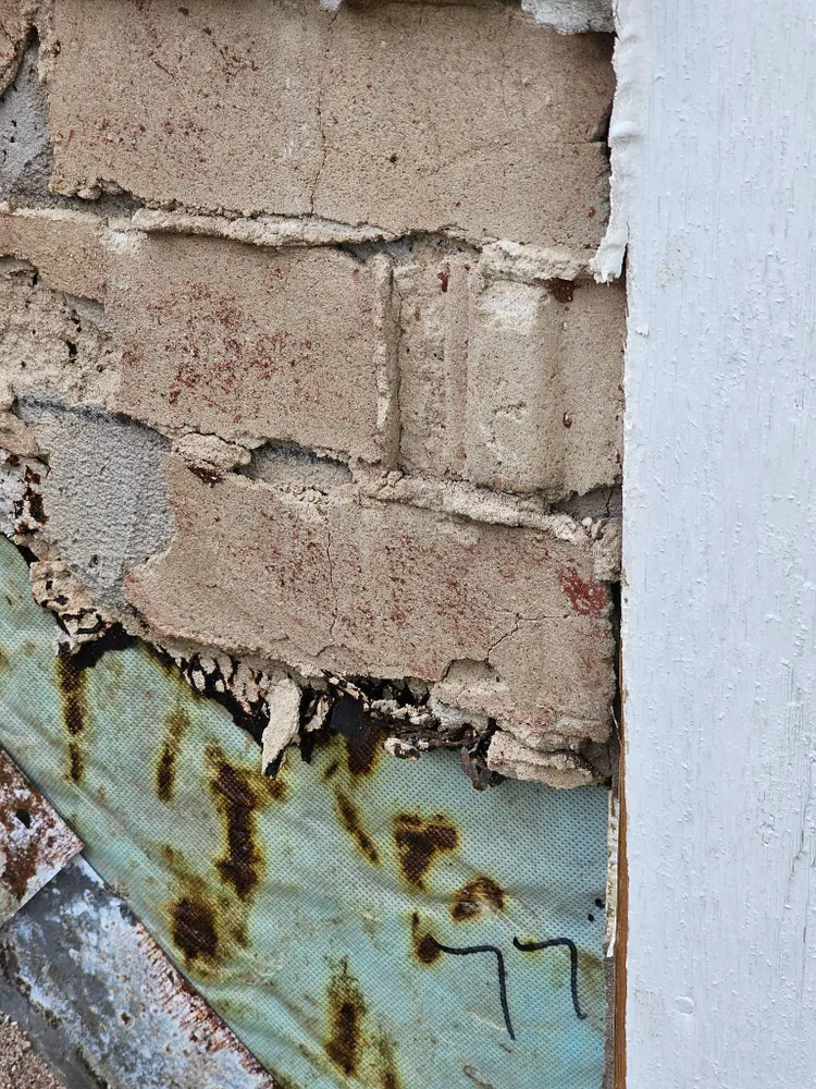 Workers on a tall scaffold next to a house with brick and a garage door, under a cloudy sky.