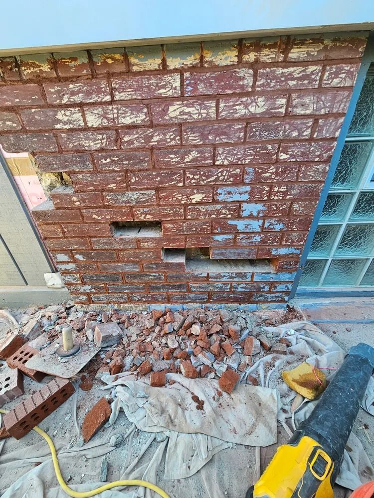 Brick wall being dismantled; red bricks, debris on tarp, and tools.