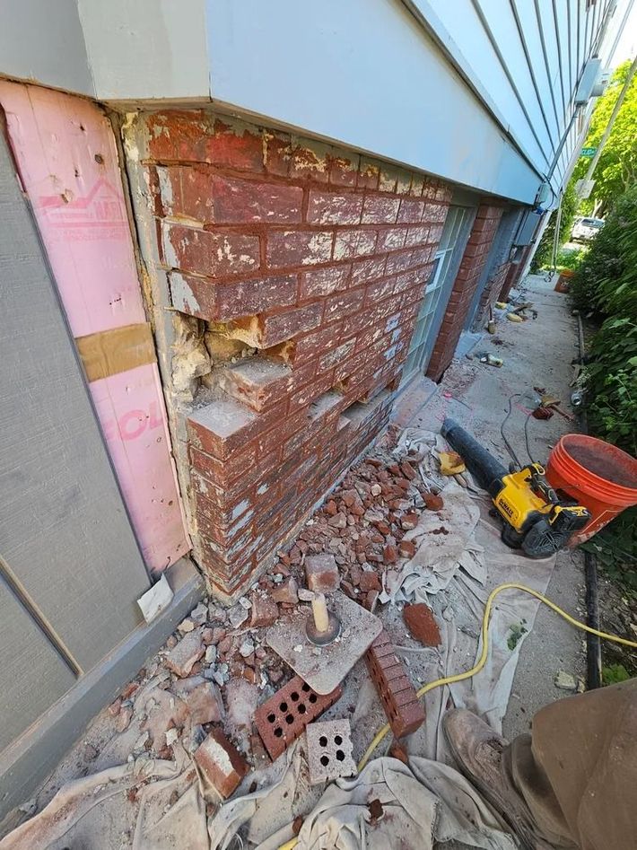 Brick wall damage during home repair. Red bricks crumbling, debris on ground, pink insulation visible.