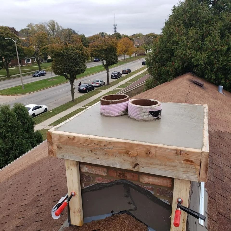 Chimney repair on a rooftop with freshly poured concrete. Two cylindrical chimney flue caps are visible.