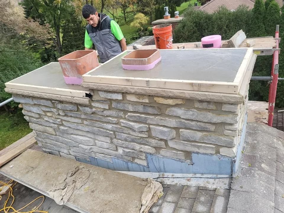 Man working on a stone chimney. Concrete poured on the top, scaffolding, and mortar visible.
