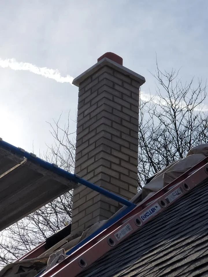 Brick chimney with a red cap on a rooftop, with a blue sky background.