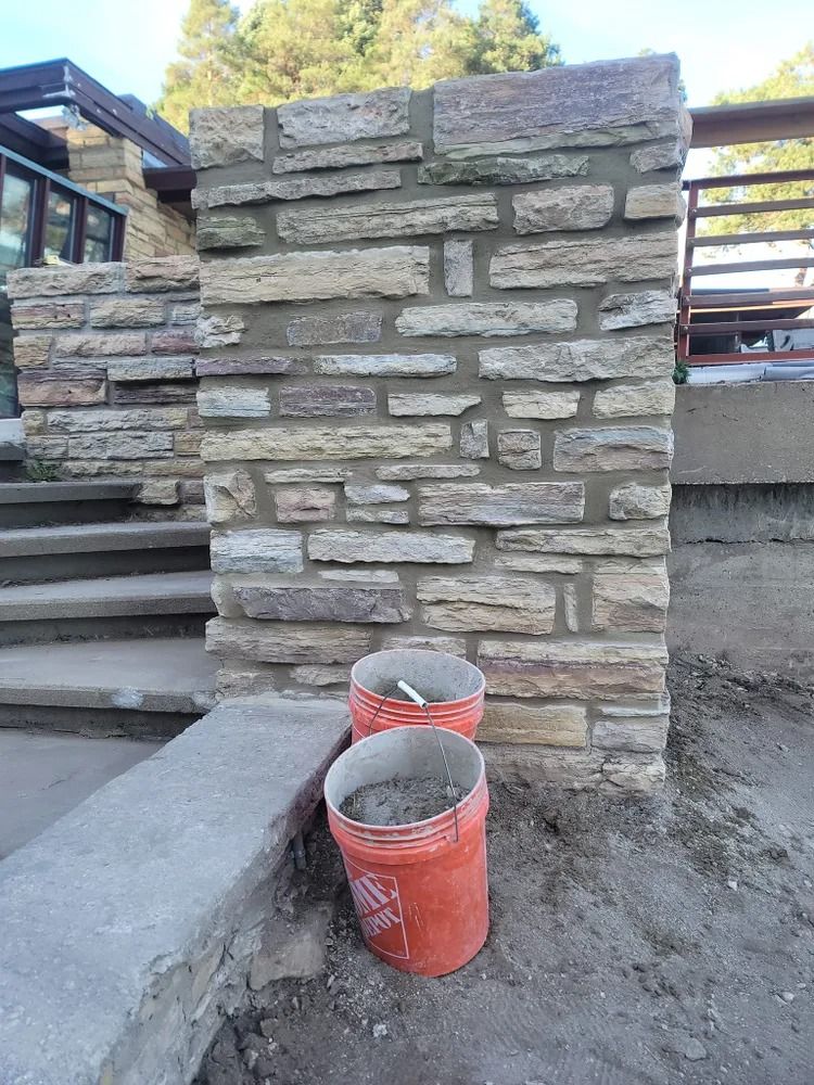 Stone pillar with two orange buckets in front, beside a concrete step and low wall.