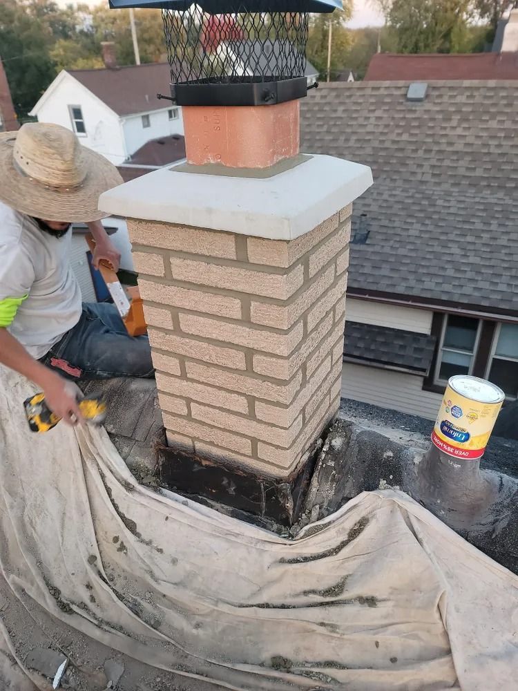 Person working on a brick chimney with tools and a tarp on a rooftop.