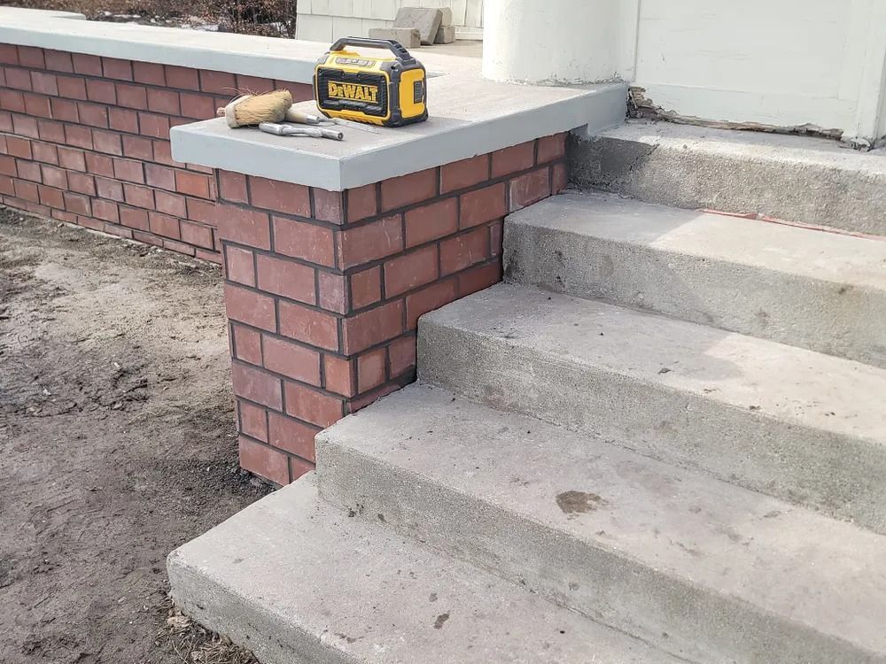 Brick and concrete steps leading to a building with brick accents and a power tool on a ledge.