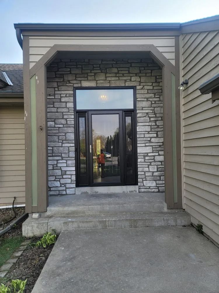 Two workers on scaffolding repairing a brick house. Red buckets stacked on the ground.