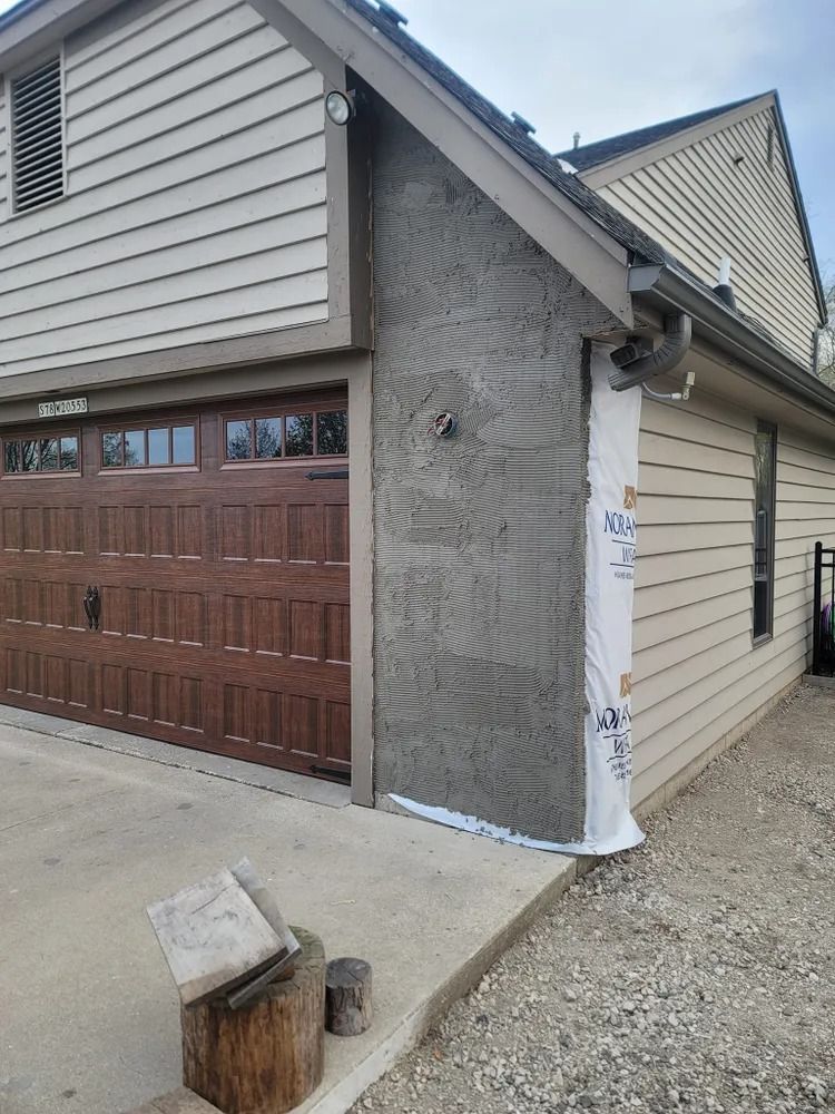 Garage exterior with brown door, tan siding, and a section of wall covered in stucco.