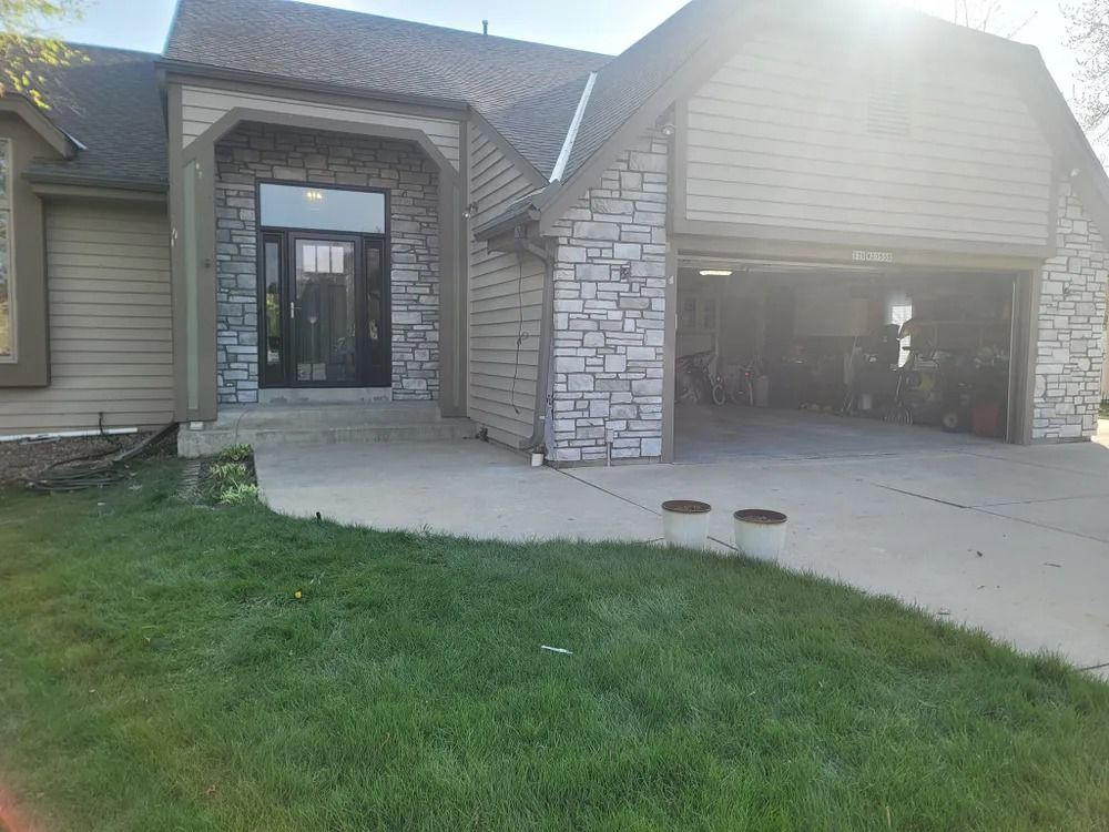 House exterior with stone facade around the front door and garage. Green lawn, concrete driveway.