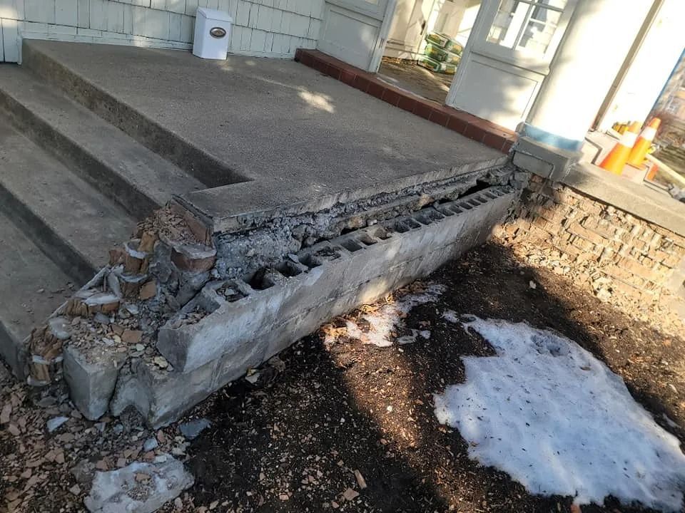 Damaged concrete steps and landing outside a building, with exposed cinder blocks and debris.