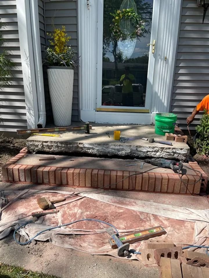 Brick steps being rebuilt outside a home. One step is concrete, with tools and a worker visible.