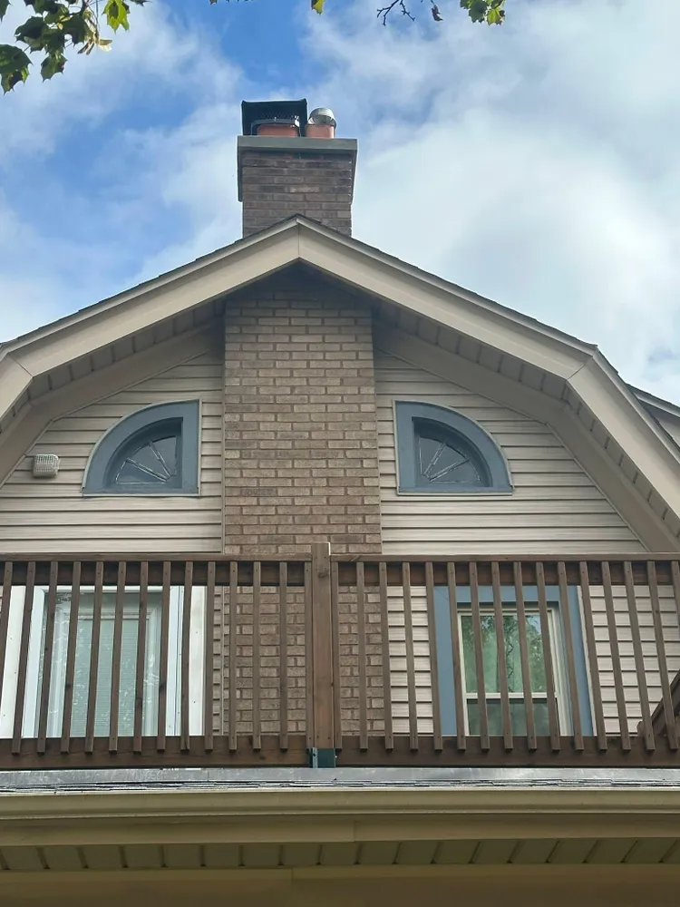 Exterior of a house with a brick chimney, a balcony, and arched windows. Blue sky visible.