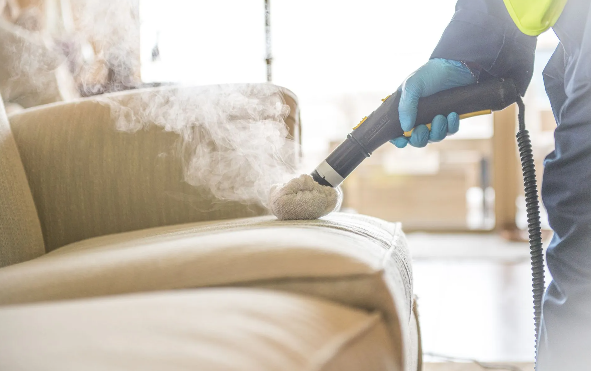 A person is cleaning a couch with a steam cleaner.