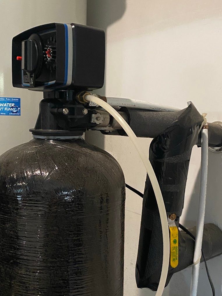 Water treatment tank with black control valve and white tubing mounted on top.