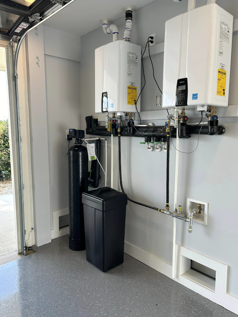 Two wall-mounted white water heaters in a utility room with pipes and a trash bin.