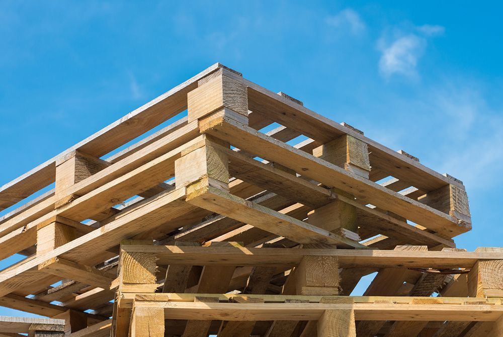 Stacked wooden shipping pallets against a bright blue sky.