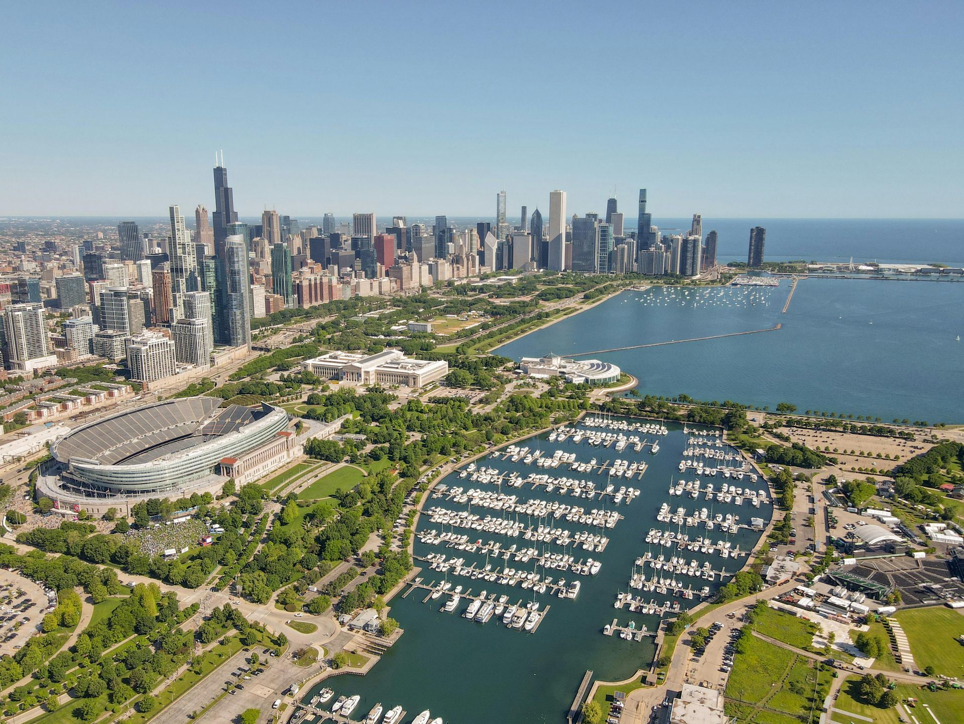 Aerial view of the Chicago skyline, Soldier Field, and the Burnham Harbor marina along Lake Michigan on a sunny day.
