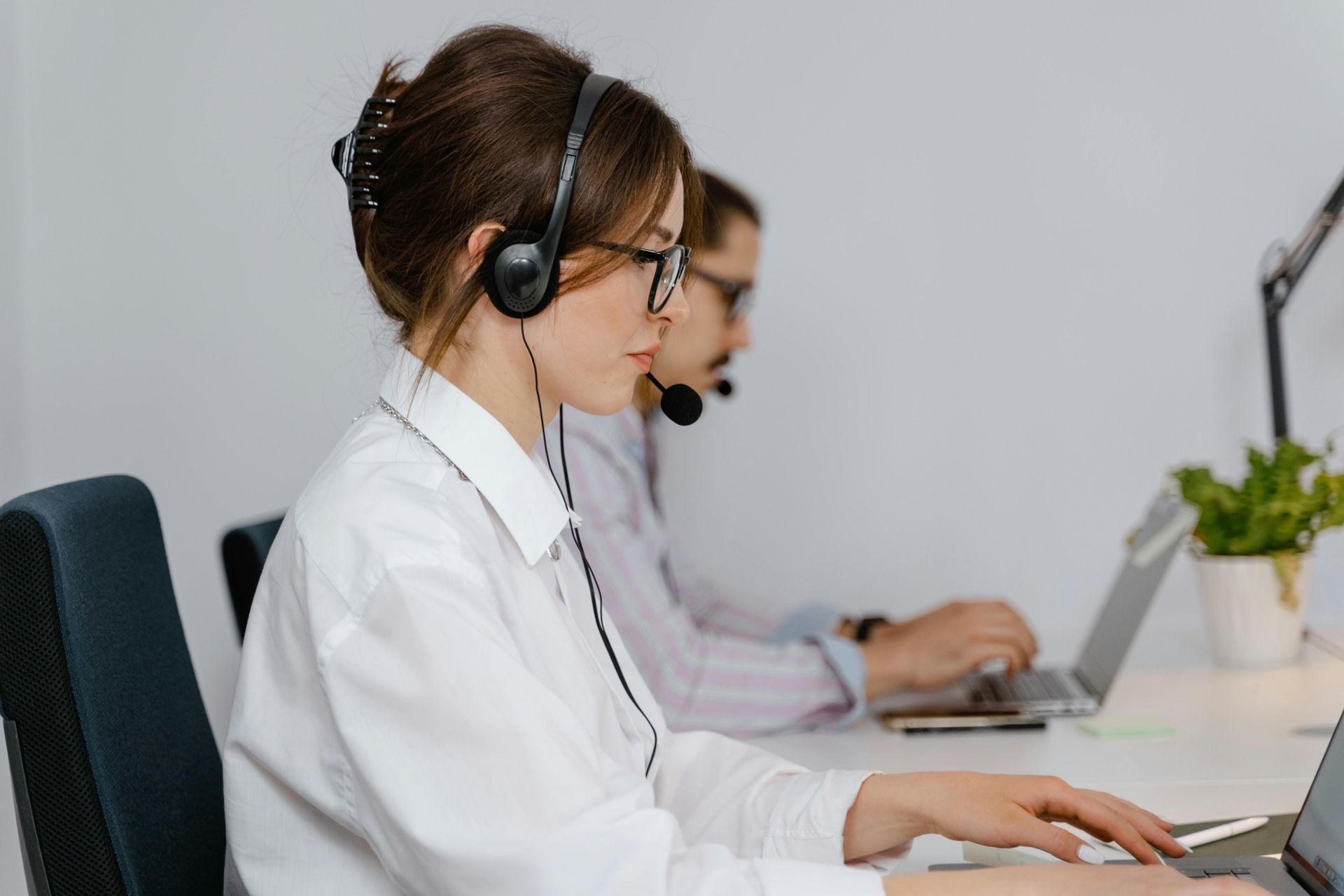 Two customer support agents with headsets sit in a bright office working at laptops.