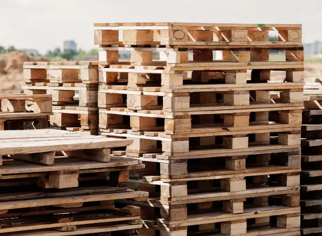A large, neat stack of weathered wooden pallets sitting in an outdoor construction area.