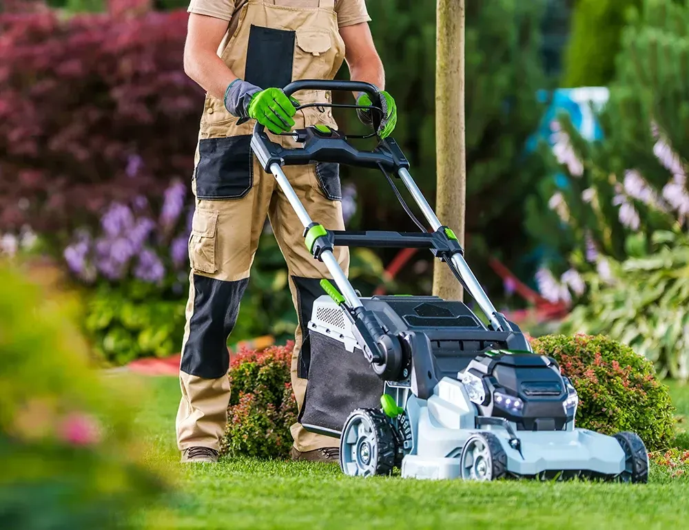 A man is standing next to a lawn mower on a lush green lawn.