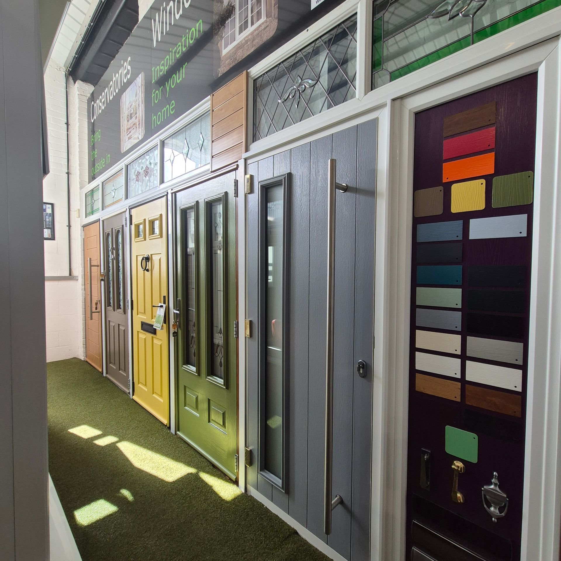 Several colorful doors on display in a showroom, with paint swatches and hardware samples.