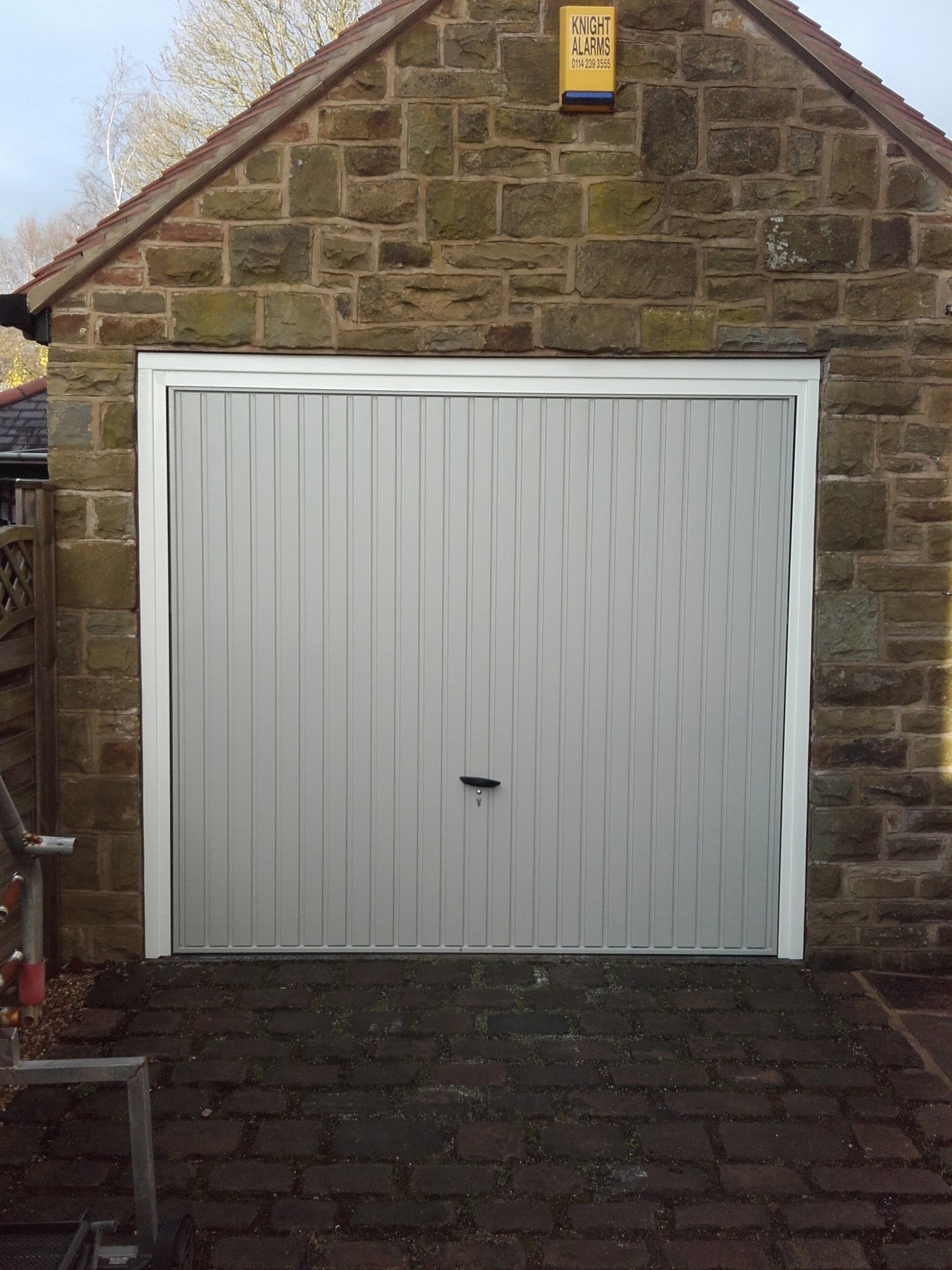 A light gray garage door with a white frame, set in a stone building.