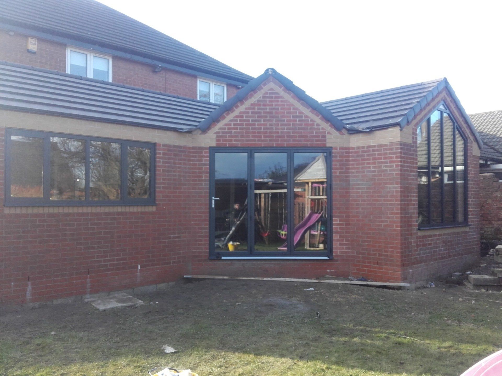 Red brick home extension with dark gray windows and doors.