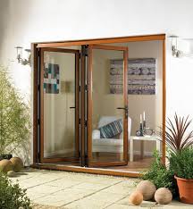 Brown-framed glass doors open to a well-lit interior with a chair, candles, and artwork. Outdoor setting with greenery.