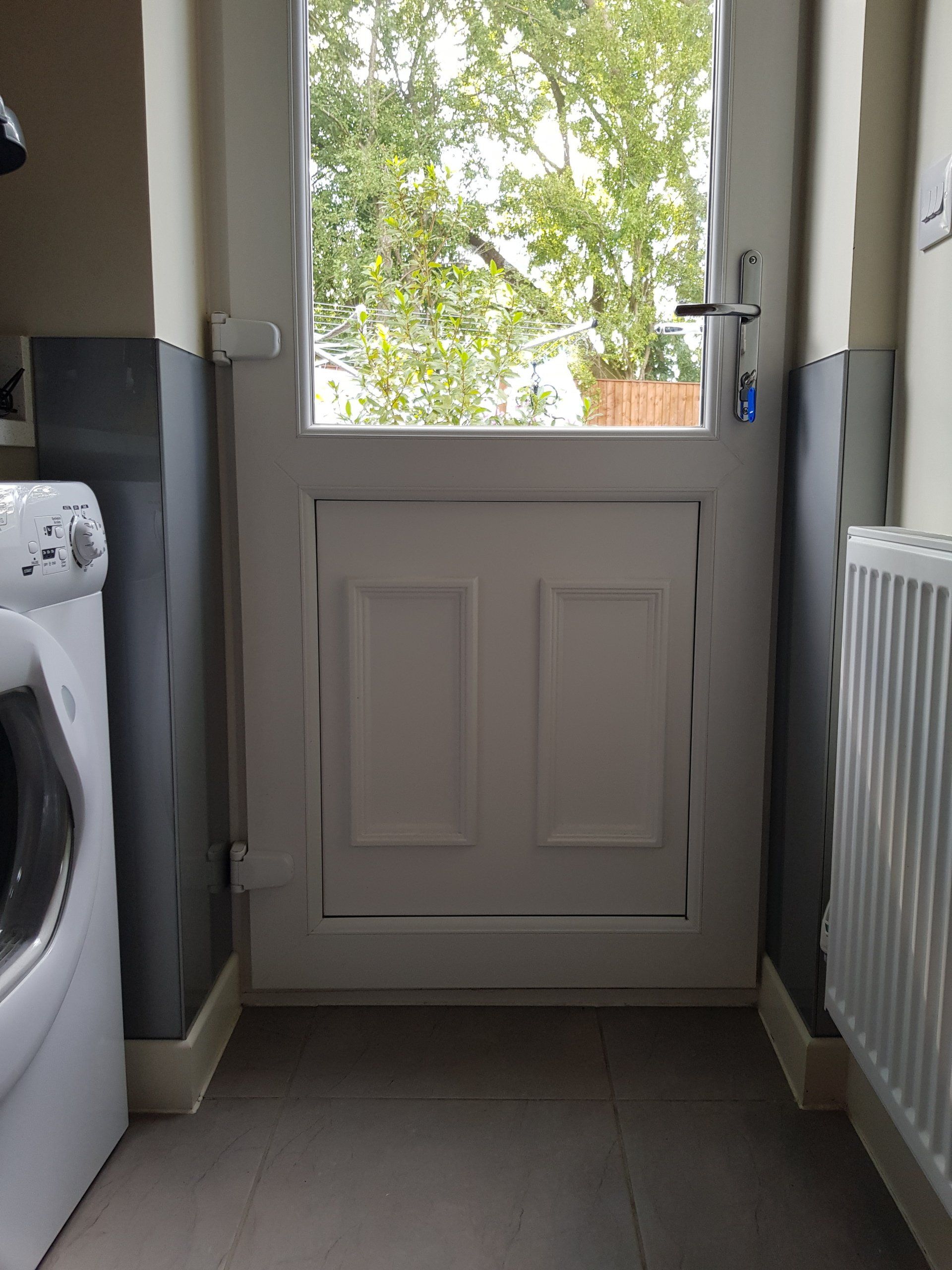 White dutch door with glass window above, between gray walls, washing machine left, radiator right, exterior view.