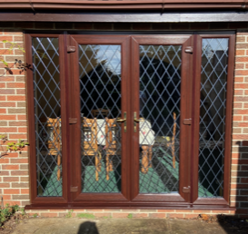 Brown diamond-paned French doors on brick wall, reflecting indoor furniture.