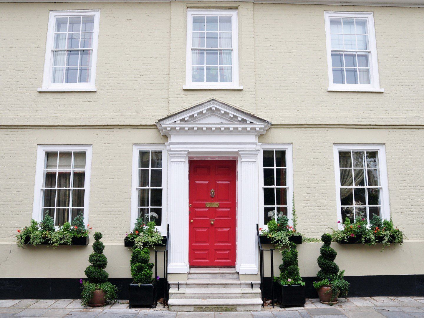 Cream-colored house with red front door, white trim, and window boxes filled with greenery.