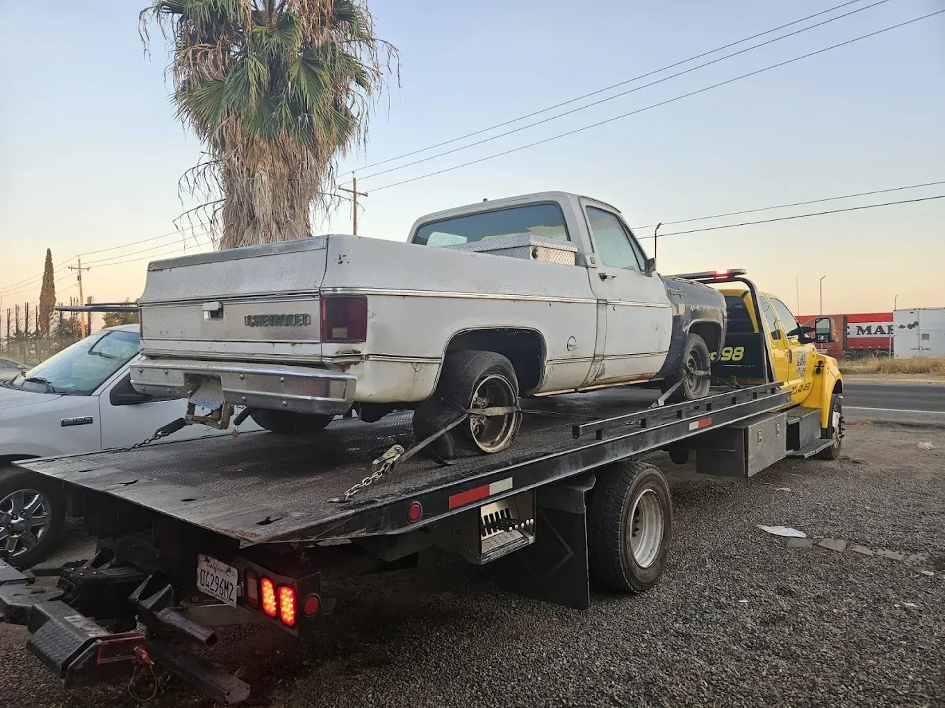 A white Chevrolet pickup truck secured on the bed of a yellow flatbed tow truck in an outdoor lot.