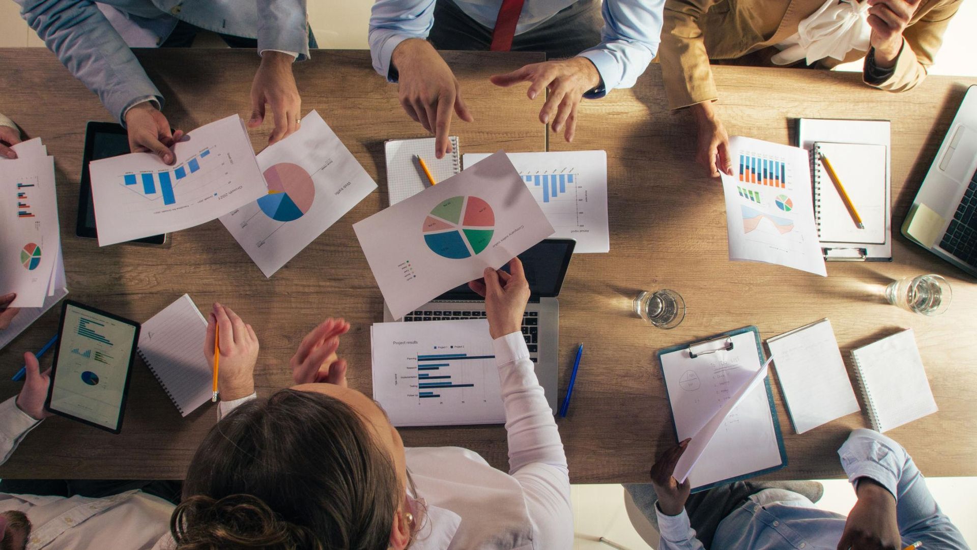 People around a table reviewing colorful charts and graphs during a collaborative meeting.