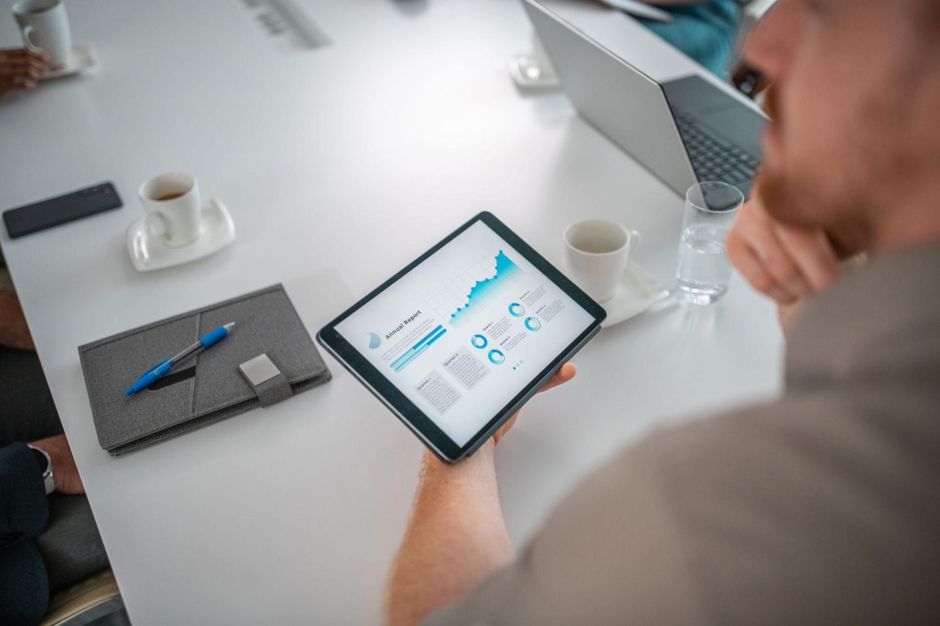 Person holding a tablet showing analytics charts at a white office desk