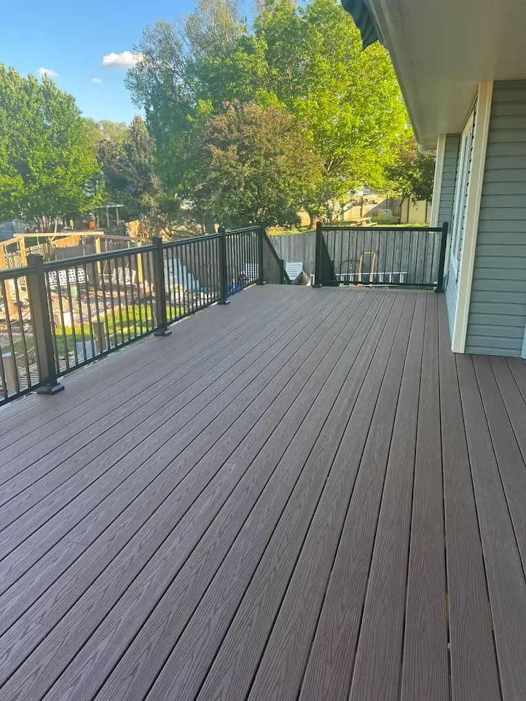A large wooden deck with a metal railing on the side of a house.