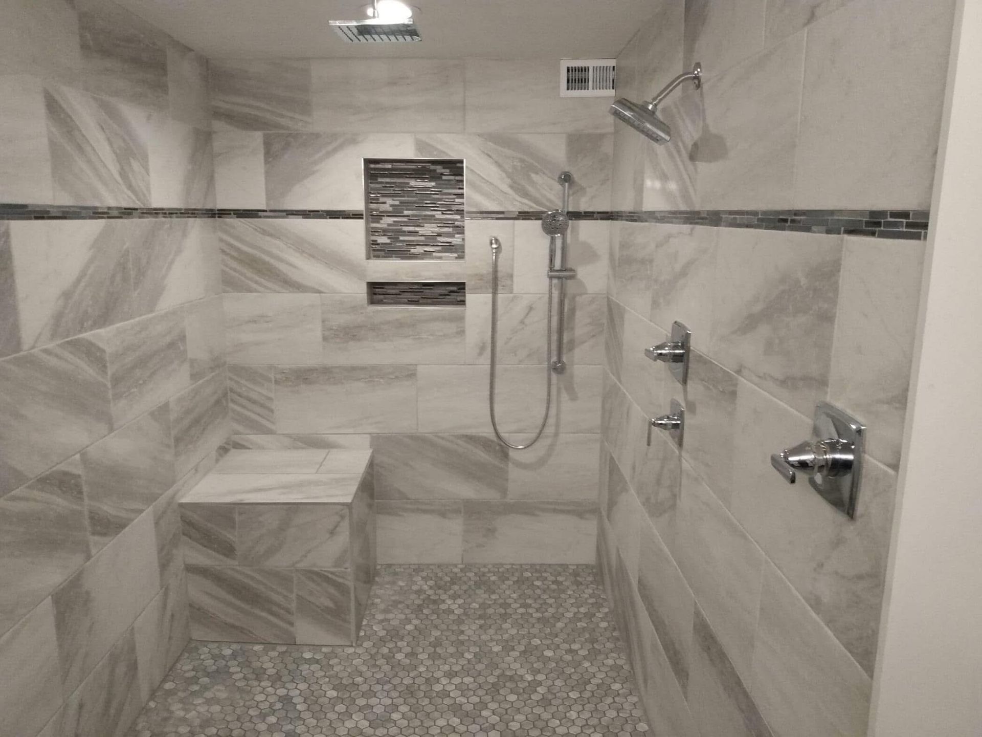 A black and white photo of a walk in shower with a bench.