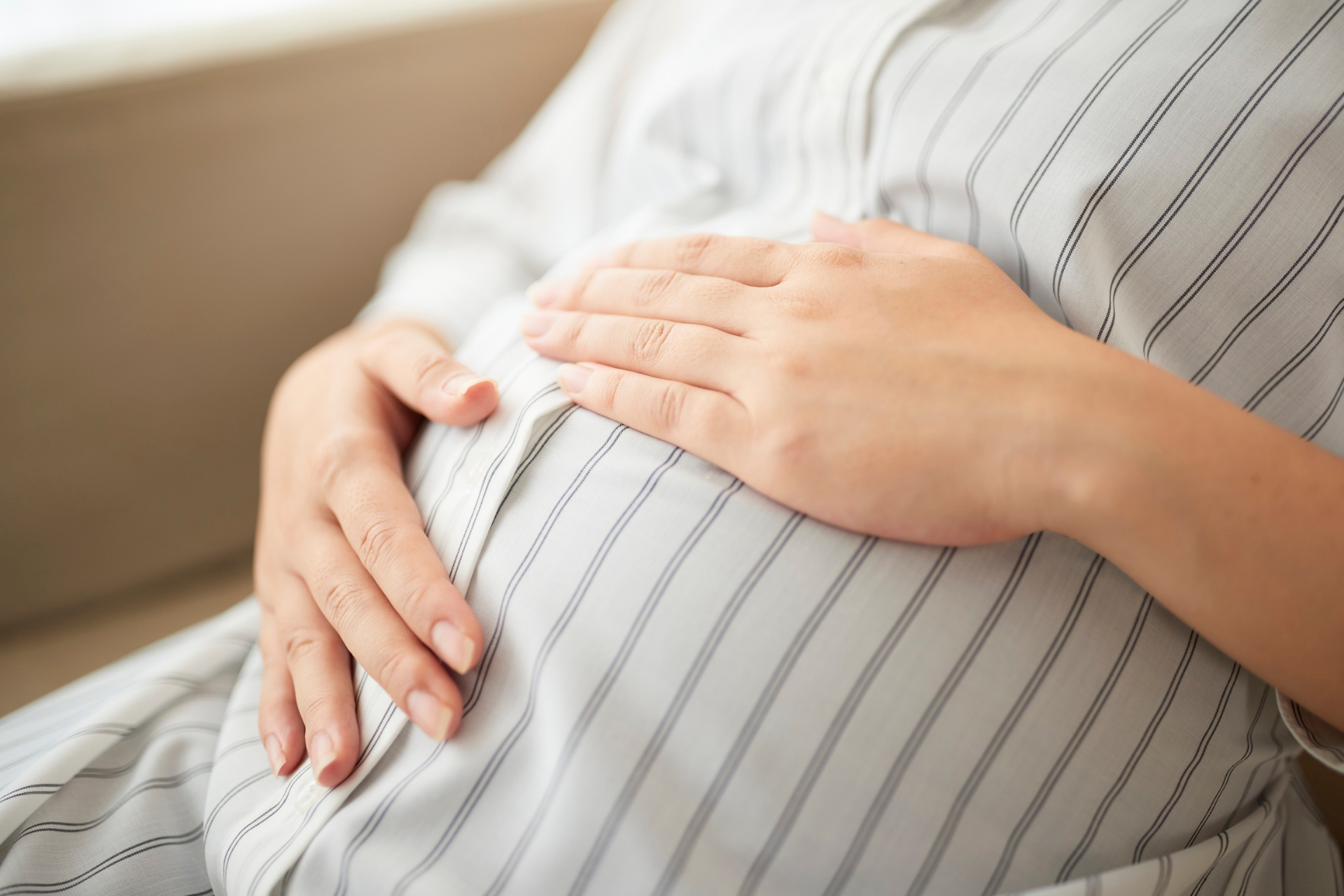 A pregnant woman sits calmly, hands on her belly, practicing safe pregnancy practices and self-care. 