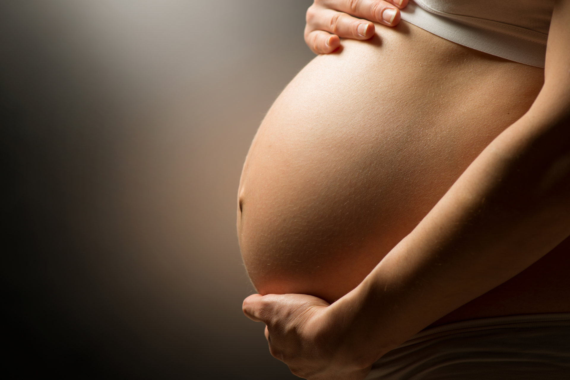 A woman having a fall pregnancy cradles her belly in the warm light of the morning sun.