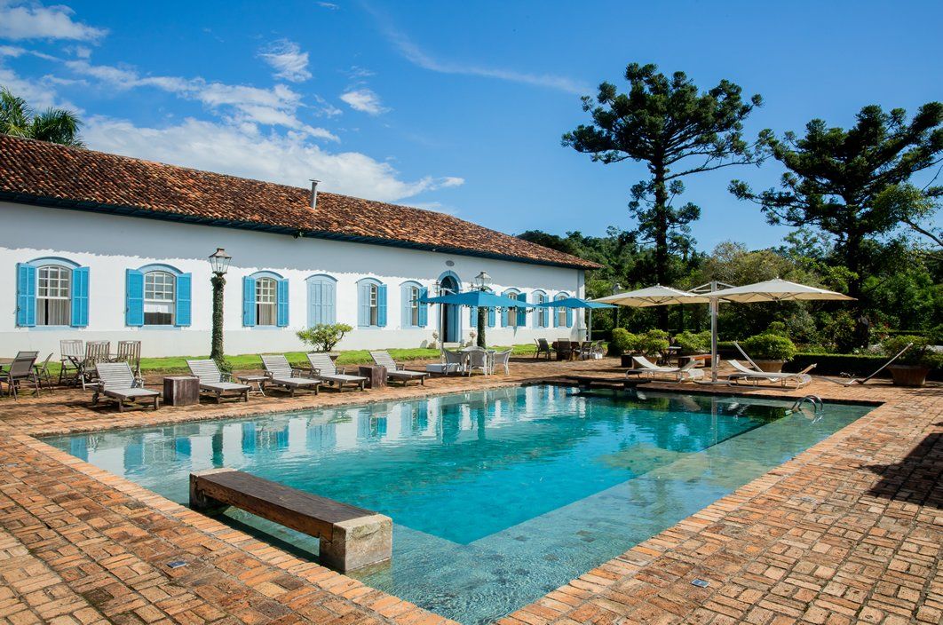 Uma grande piscina cercada por cadeiras e guarda-sóis em frente a um prédio branco.