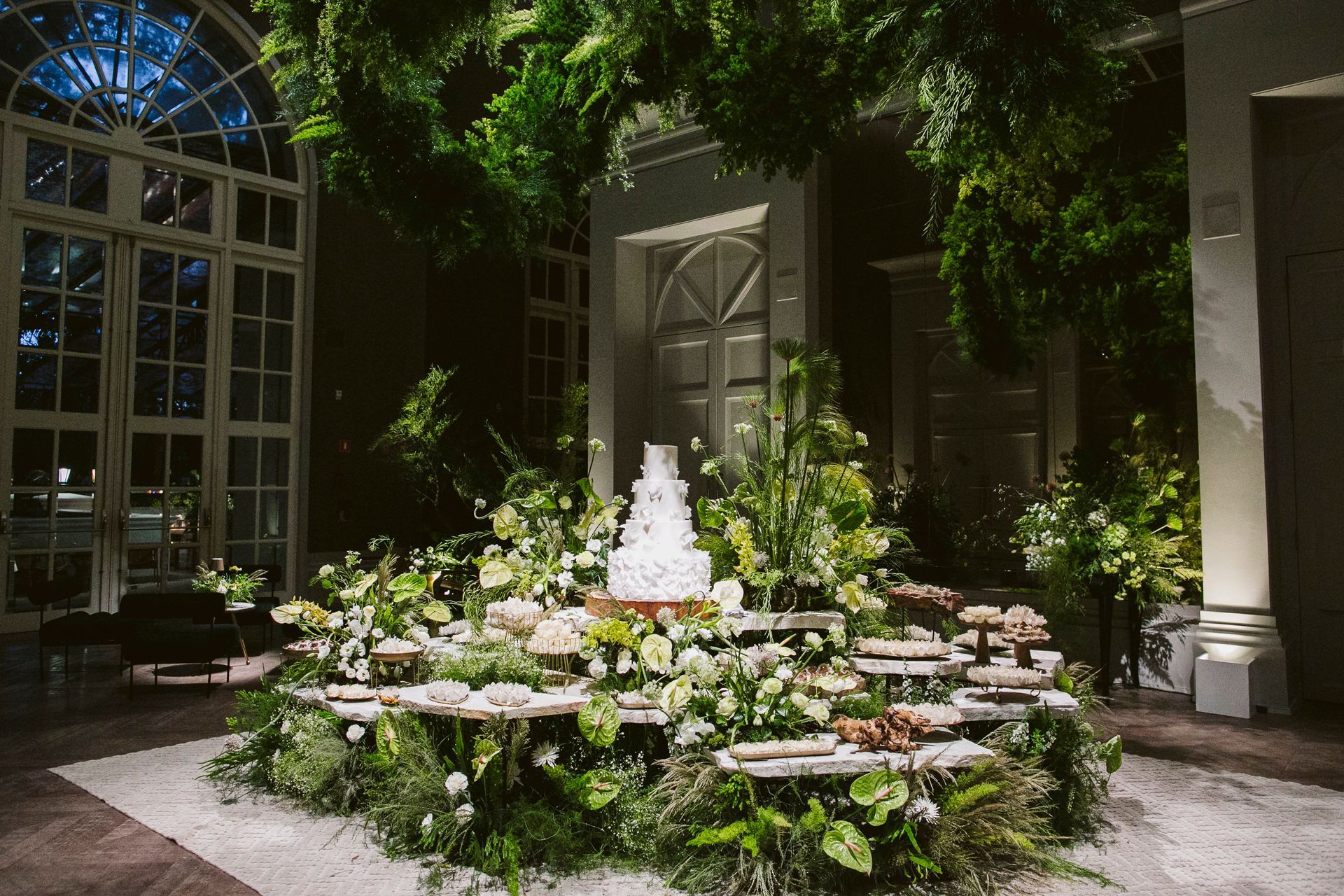 Um bolo de casamento está sobre uma mesa cercada por plantas.