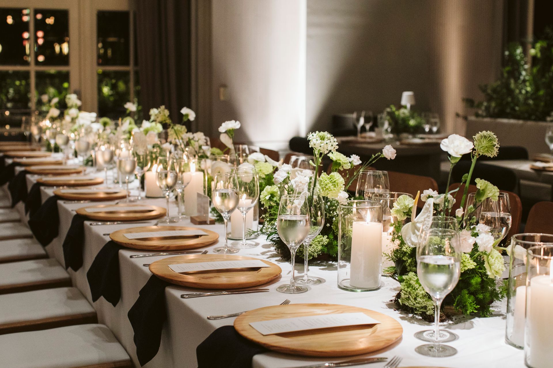 Uma longa mesa com pratos, copos, velas e flores.