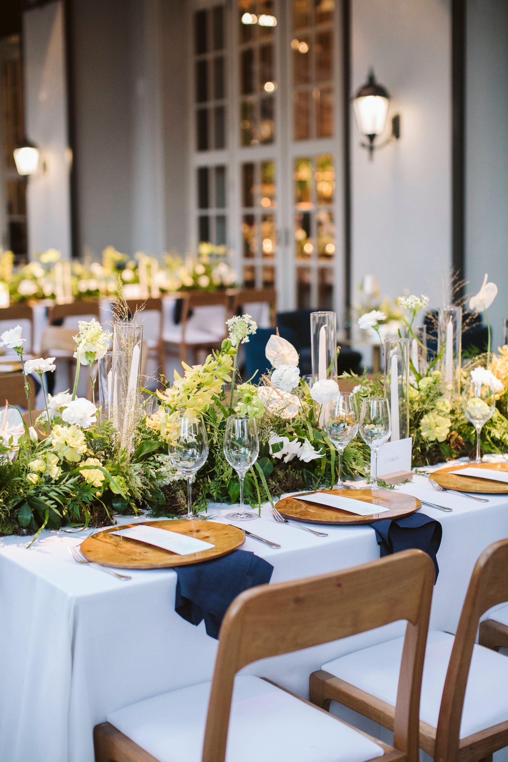 Uma longa mesa com pratos, copos e flores sobre ela.