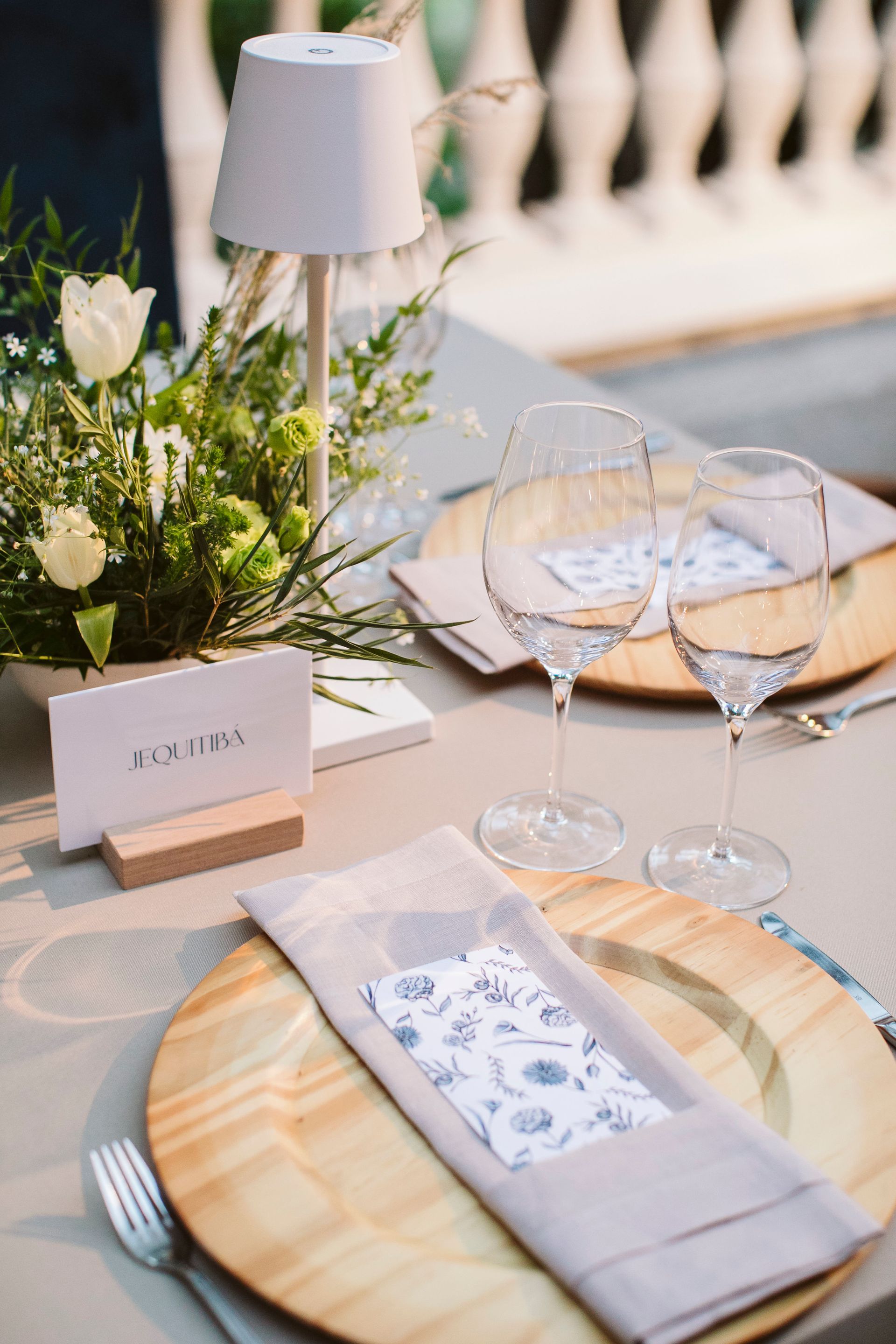 Uma mesa posta para uma recepção de casamento com pratos, copos, guardanapos e um abajur.