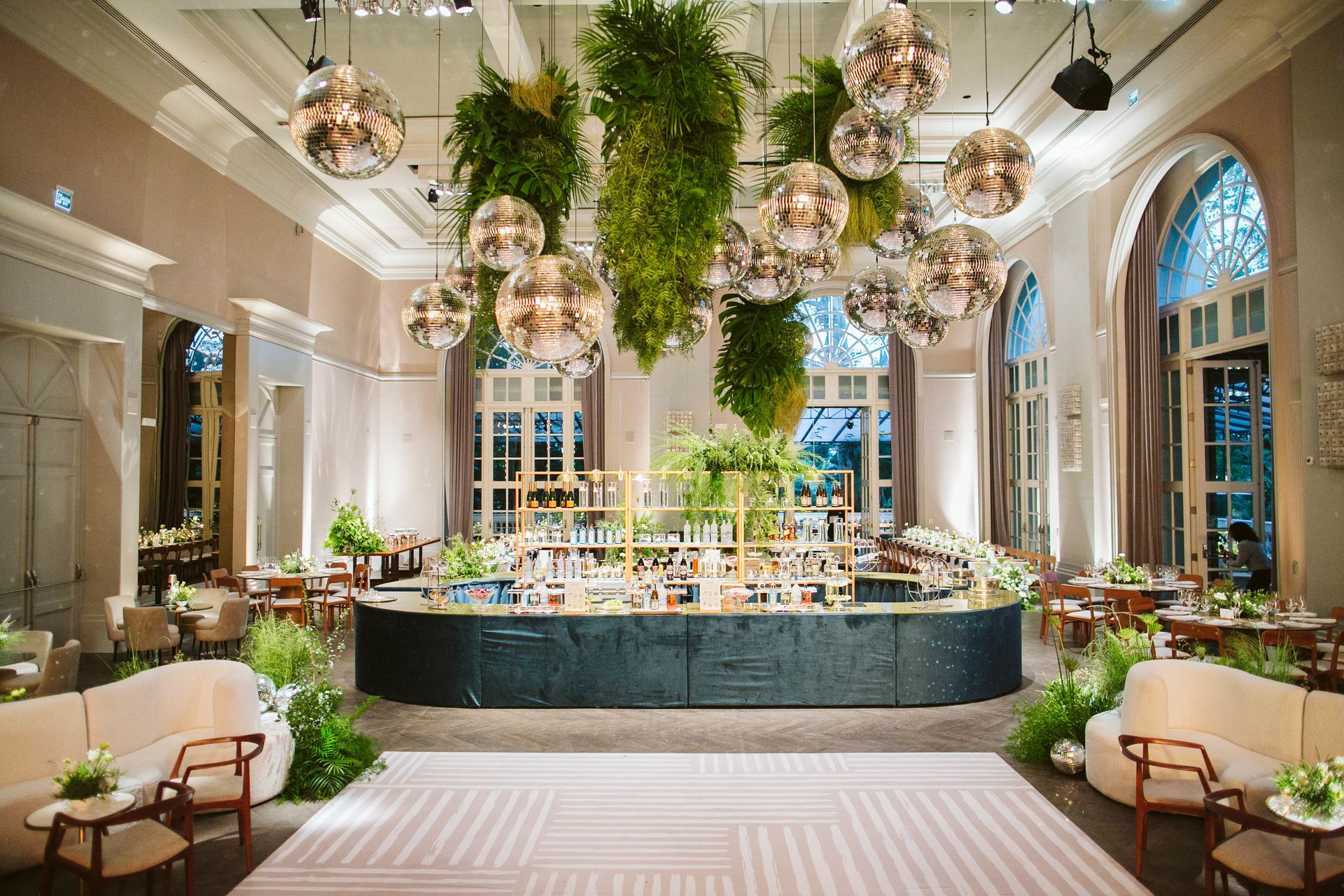 Uma sala grande com pista de dança, mesas, cadeiras e plantas penduradas no teto.