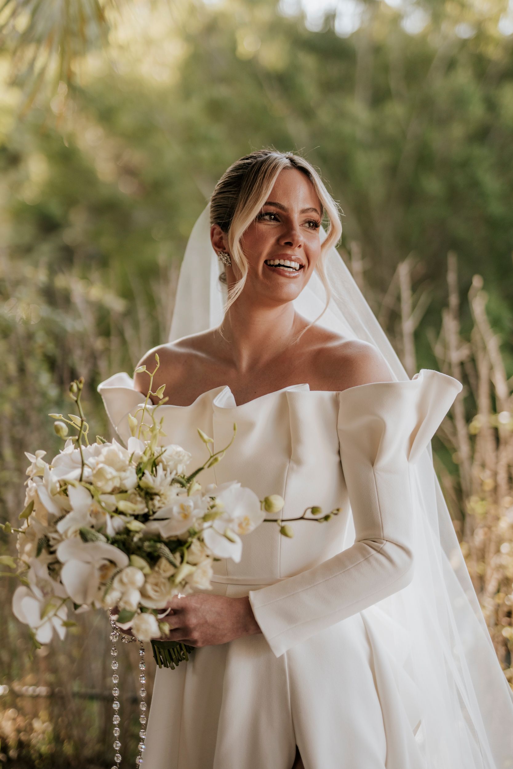 Uma noiva com um vestido e véu brancos está segurando um buquê de flores brancas.