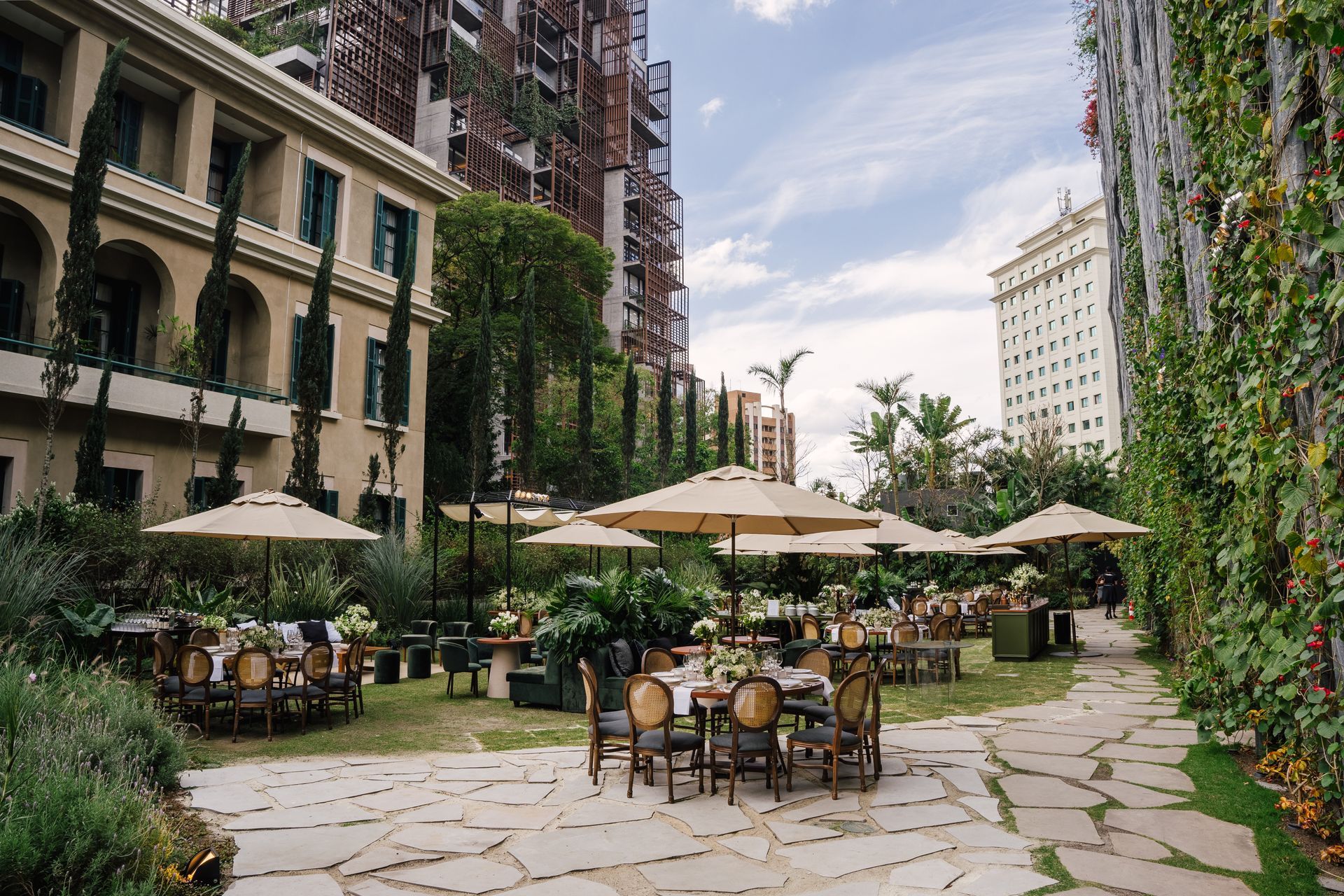 Um pátio com mesas, cadeiras e guarda-sóis em frente a um prédio.