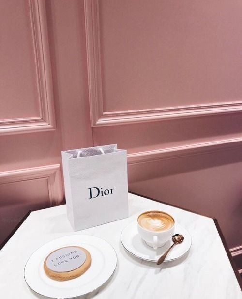 Uma mesa com uma xícara de café, um biscoito e uma bolsa Dior.