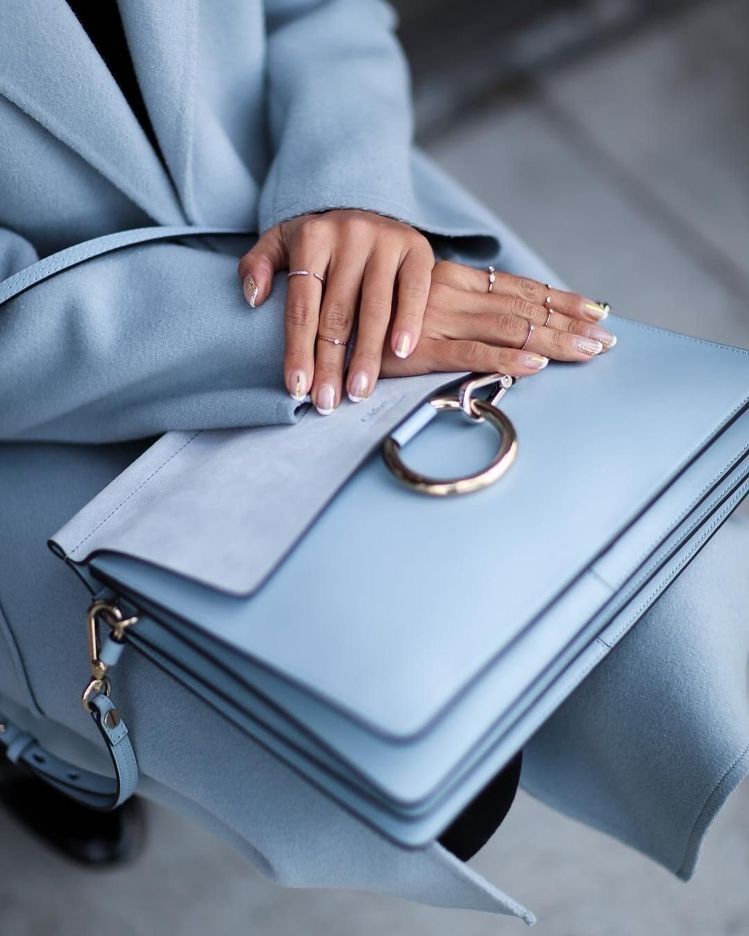 Uma mulher com um casaco azul claro está segurando uma bolsa azul clara